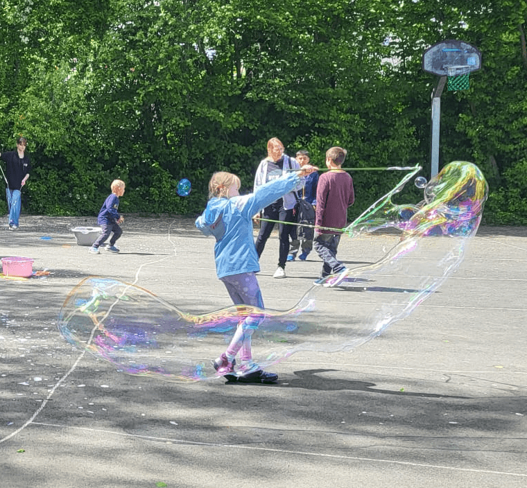 Ein Mädchen auf einem grauen Basketballplatz mit einer riesigen Seifenblase, Menschen im Hintergrund