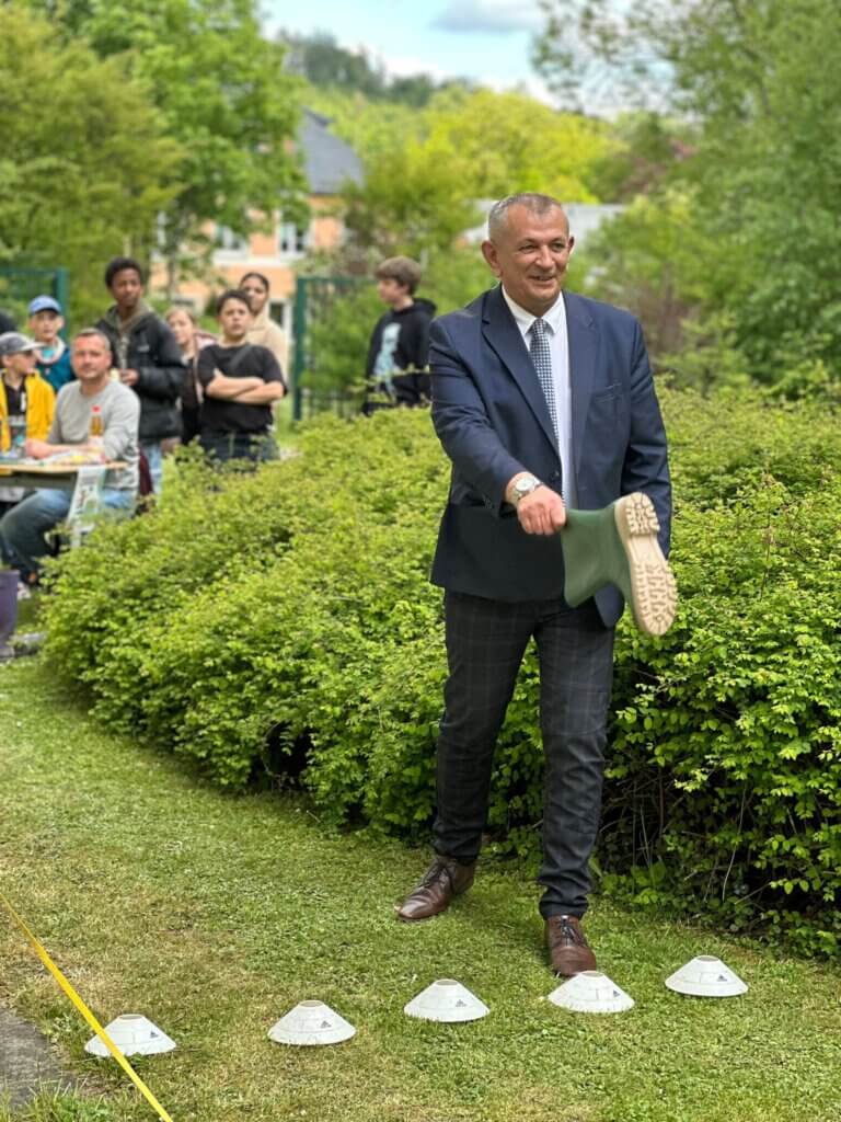 Ein Mann mit einem Gummistiefel in der Hand in Anzug, Menschen im Hintergrund