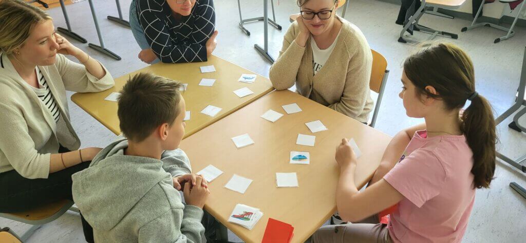 5 Personen sitzen um einen Tisch und spielen Memory