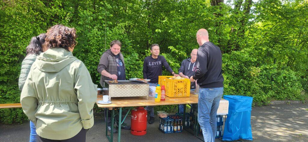 Ein Mann kauft eine Bratwurst an einem Stand mit 3 Personen, links stehen noch 2 Frauen