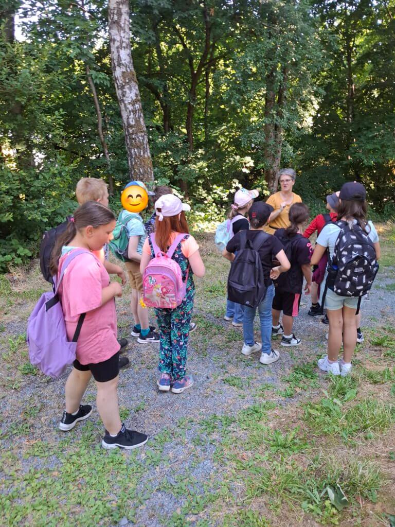 Kinder stehen um eine Frau in einem Wald und hören der Frau zu