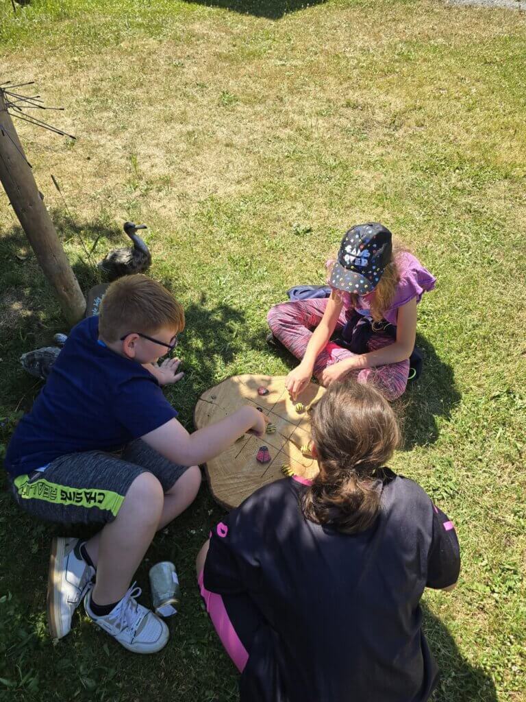 3 Kinder spielen auf einer Holzscheibe ein Spiel mit Käfern und Bienen