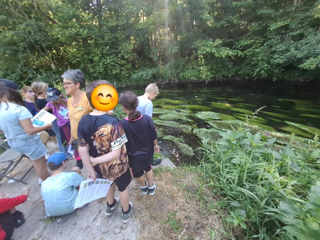 Kinder stehen an einem Flusslauf mit einer Frau