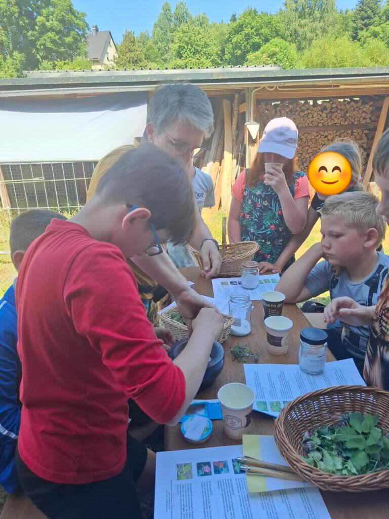 Kinder stehen mit einer Frau um einen Tisch und mischen Kräutersalz an