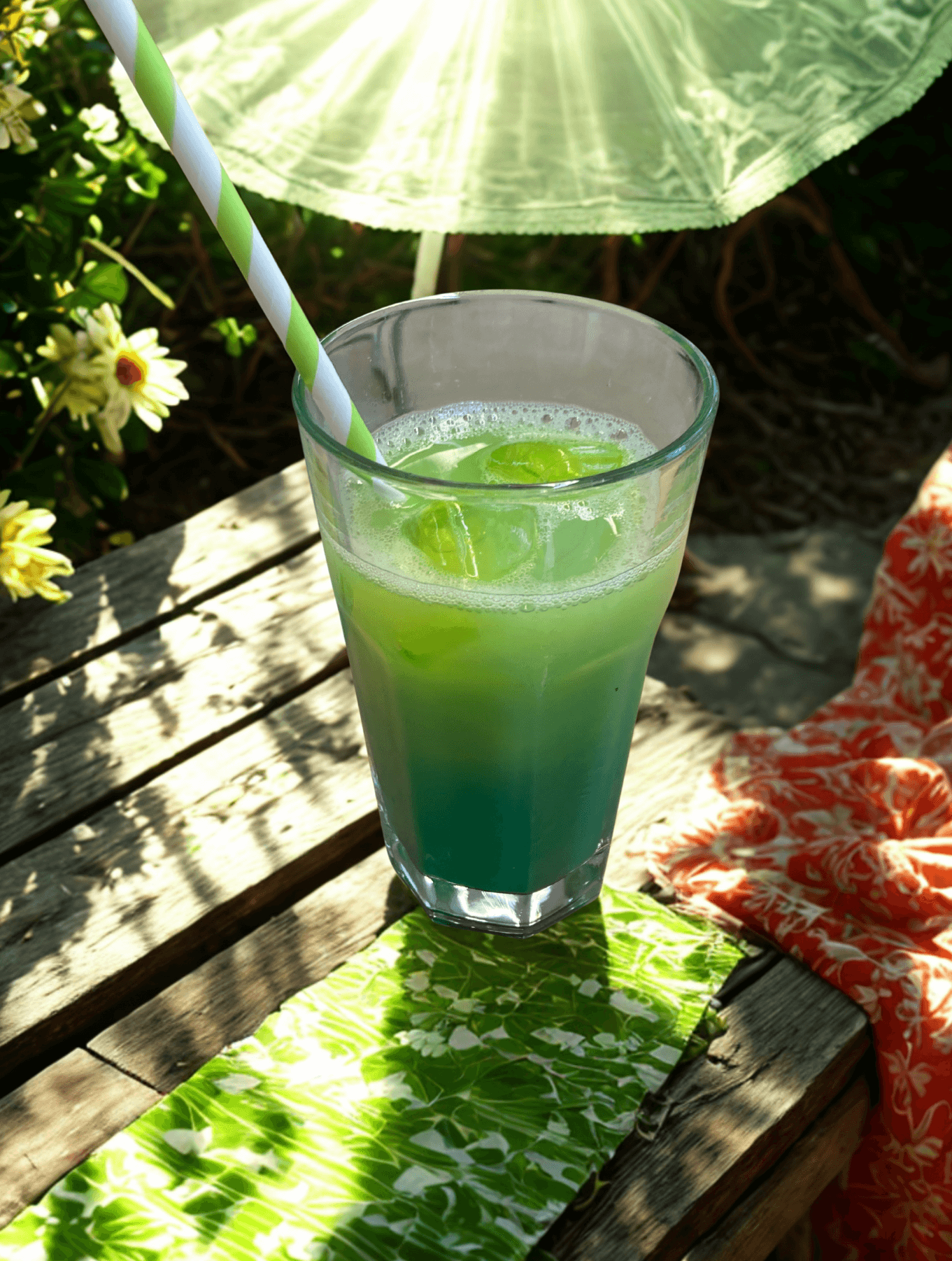 Ein grüner Cocktail mit einem Strohhalm steht auf einem Holztisch im Garten