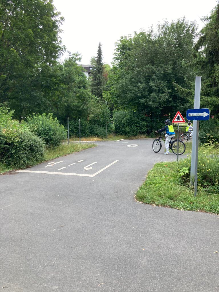 Ein Junge biegt auf dem Verkehrsübungsplatz ab. 2 Verkehrssschilder sind zu sehen