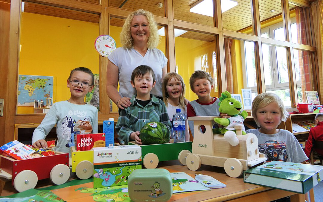 5 Kinder und eine Erzieherin stehen an einem Tisch mit Materialien zum Programm Jolinchen Kids